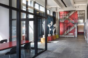 Moderne entreehal aan de Generaal Vetterstraat met glazen wanden, kleurrijke accenten, opvallende trappen en kunstzinnige bloemeninstallatie.